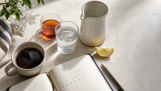 Hydration station with coffee, tea, water glass, ceramic pitcher, and daily beverage rhythm on a bright kitchen counter.