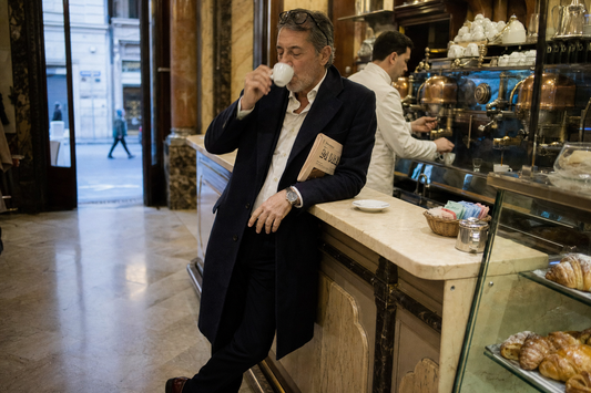 Italian espresso bar ritual with a businessman standing at a marble counter, barista, pastries, and morning cafe light.